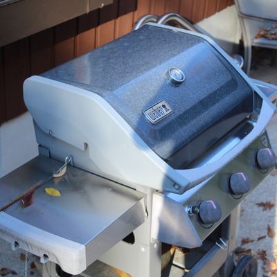 Sale Photo Thumbnail #27: Weber Genesis liquid propane gas grill featuring a built-in lid thermometer, stainless steel side shelves, and three burner control knobs.