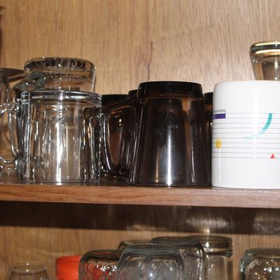 Sale Photo Thumbnail #65: Collection of assorted glassware and mugs, including clear glass beer mugs, smoky brown glass cups, a promotional stainless steel tumbler, and graphic ceramic mugs.