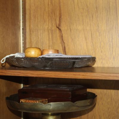 Sale Photo Thumbnail #49: Assorted vintage items displayed inside a wooden cabinet, including a clear pressed glass tray with napkin rings and a brass pedaled dish holding small boxes.