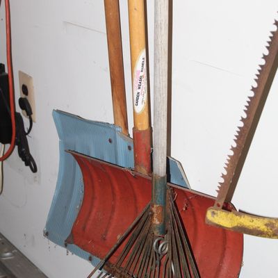 Sale Photo Thumbnail #141: Collection of vintage lawn and garden tools hanging on a wall, including snow shovels, a metal leaf rake, a Garden Weasel handle, and a bow saw.