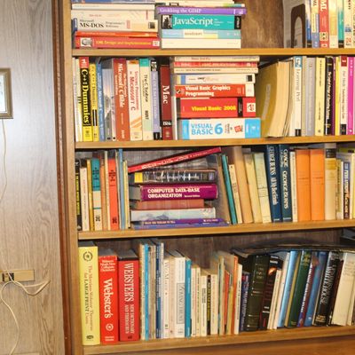 Sale Photo Thumbnail #122: A wooden bookcase filled with computer programming manuals, reference books, and novels alongside a vintage square wall clock.