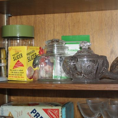 Sale Photo Thumbnail #61: Assorted vintage kitchenware including a stainless steel food chopper, Feemster's Famous Vegetable Slicer in original box, and clear glass jars and candy dishes.