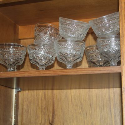 Sale Photo Thumbnail #48: Collection of vintage clear pressed glass dessert cups stacked on a shelf in an oak cabinet.