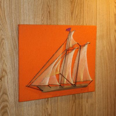 Sale Photo Thumbnail #94: Vintage 1970s nautical sailboat string art piece mounted on an orange fabric backing.