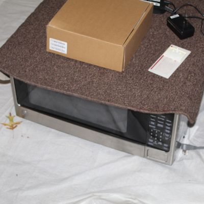 Sale Photo Thumbnail #136: GE stainless steel countertop microwave oven with digital keypad, displayed with a cardboard box and power adapters resting on top.