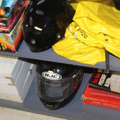 Sale Photo Thumbnail #104: Metal shelving unit containing helmets, including a black HJC full-face motorcycle helmet, vintage science kit boxes, and stamp collecting supplies.