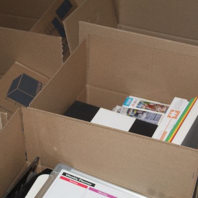 Sale Photo Thumbnail #145: Cardboard moving boxes filled with assorted household items, including a weekly planner whiteboard, jigsaw puzzles, and books.