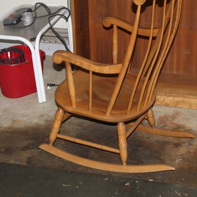 Sale Photo Thumbnail #138: Vintage light maple Windsor-style rocking chair featuring turned legs and spindle back, shown alongside a small side table and a red bucket.