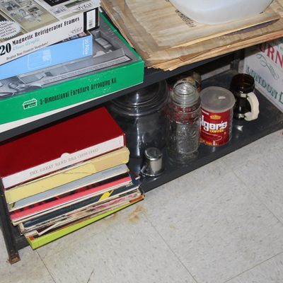 Sale Photo Thumbnail #108: Metal shelving unit containing various household goods, including a vintage Folgers coffee tin, glass jars, record box sets, and magnetic refrigerator frame sets.