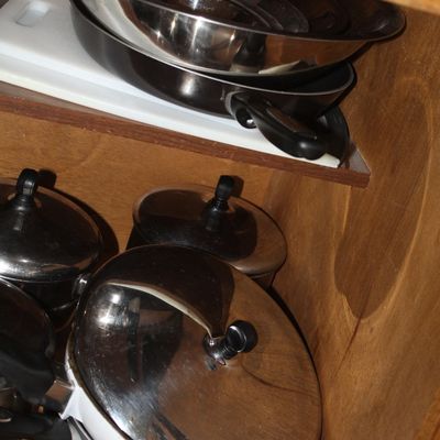 Sale Photo Thumbnail #71: Collection of stainless steel cookware, including frying pans and lidded saucepans, stacked inside a wooden cabinet.