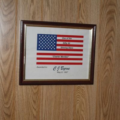 Sale Photo Thumbnail #117: Framed award certificate featuring an American flag motif, presented to C J Byrne on May 8, 1997, in a dark wood frame.