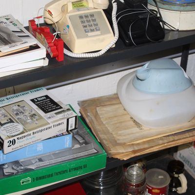 Sale Photo Thumbnail #107: Metal shelving unit holding a collection of vintage household items, including a beige push-button telephone, books, magnetic photo frames, and a cool-mist humidifier.