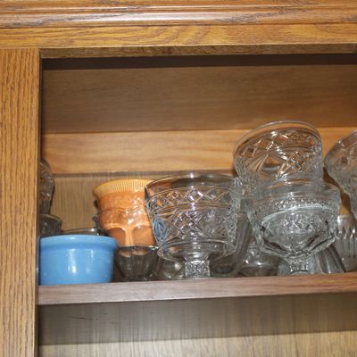 Sale Photo Thumbnail #47: Collection of clear pressed glass dessert cups and small colorful ceramic ramekins stacked inside a wooden cabinet.