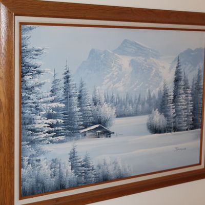 Sale Photo Thumbnail #34: Framed winter landscape oil painting featuring a snowy pine forest, cabin, and mountain backdrop in a stained wood frame.