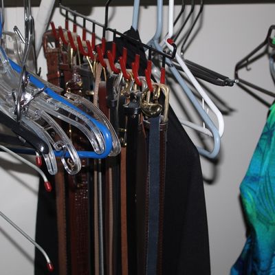 Sale Photo Thumbnail #20: Collection of leather belts stored on a hanging belt rack alongside various clothing hangers in a closet.