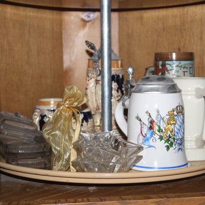 Sale Photo Thumbnail #63: Collection of German-style ceramic beer steins with lidded tops and small pressed glass ashtrays displayed on a corner cabinet lazy Susan.