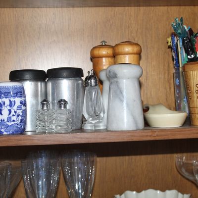 Sale Photo Thumbnail #59: An assortment of vintage kitchenware and tabletop accessories displayed on wooden cabinet shelves, including salt and pepper shakers, glass decanters, wooden mills, and stemware.