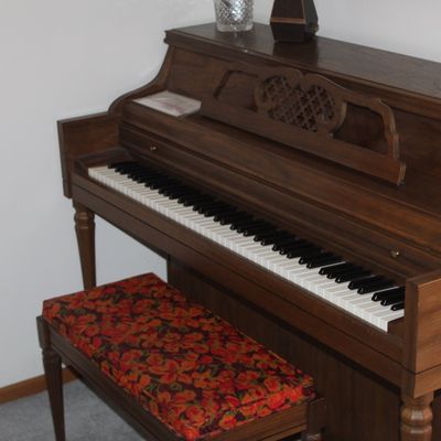 Sale Photo Thumbnail #37: Vintage dark wood spinet piano featuring an ornate music stand and a matching bench with a floral cushioned top.