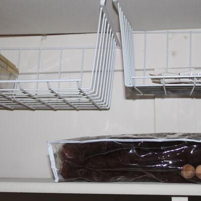 Sale Photo Thumbnail #7: Two white wire under-shelf storage baskets mounted beneath cabinet shelving alongside various household storage items.