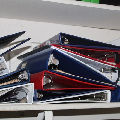 Sale Photo Thumbnail #41: Stack of assorted three-ring office binders in blue, red, and white, stored on a shelf.