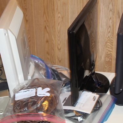 Sale Photo Thumbnail #92: Collection of computer monitors including an off-white display and two black flat screen panels, shown with bagged cables and various electronics.