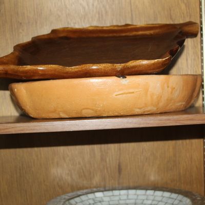 Sale Photo Thumbnail #51: A carved leaf-shaped wooden serving tray stacked on top of a terracotta dish inside a wooden cabinet.
