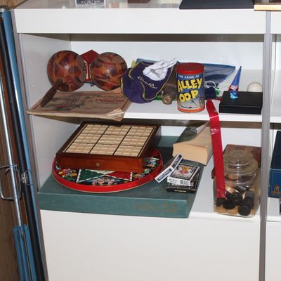 Sale Photo Thumbnail #79: Collection of vintage board games, playing cards, novelties, and a green concertina displayed on white shelving.