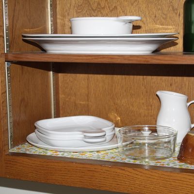Sale Photo Thumbnail #54: Assorted white ceramic serving dishes, platters, and a small pitcher stored inside an oak cabinet with floral shelf liner.