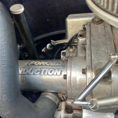 Sale Photo Thumbnail #28: Close-up view of an engine bay featuring a polished blower manifold embossed with "FORCED INDUCTION", along with rubber coolant hoses and linkages.