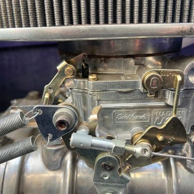 Sale Photo Thumbnail #29: Edelbrock four-barrel carburetor with dual return springs and air cleaner attached to an engine manifold.