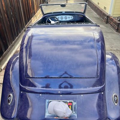 Sale Photo Thumbnail #33: Rear view of a custom dark purple hot rod roadster featuring dual exhaust pipes, teardrop taillights, and a chrome dashboard instrument panel.