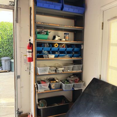 Sale Photo Thumbnail #42: Tall industrial metal shelving unit filled with organized plastic storage bins and various workshop hardware. A wall-mounted fire extinguisher is visible alongside the frame.