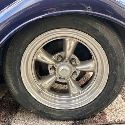 Sale Photo Thumbnail #23: American Racing five-spoke polished aluminum wheel with Bridgestone tire mounted under a dark blue vintage vehicle fender.