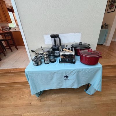Sale Photo Thumbnail #48: Collection of small kitchen appliances on a blue table, including two Crock-Pot slow cookers, a Ninja blender, a stainless steel four-slice toaster, a coffee grinder, a French press, and a spice rack.