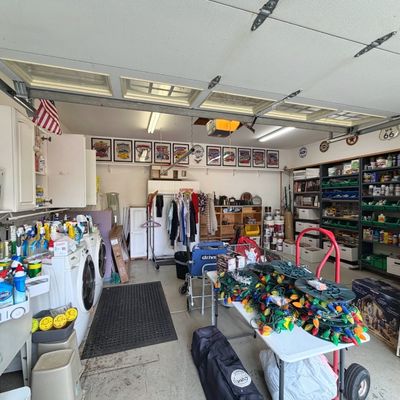 Sale Photo Thumbnail #47: Well-organized garage filled with estate sale items, including Christmas decorations, laundry supplies, tools, shelving units, and household goods.