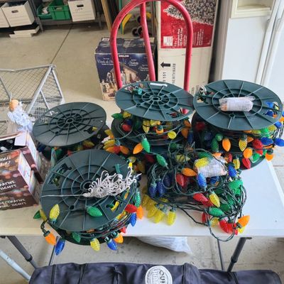 Sale Photo Thumbnail #41: Collection of multi-colored outdoor C6 and C9 Christmas light strings on spools and boxed sets displayed on a folding table.