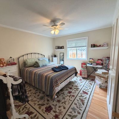 Sale Photo Thumbnail #52: Bedroom set including a metal queen bed frame with a striped quilt, a floral patterned area rug, a white quilt rack, and a white dresser with various decorative items.