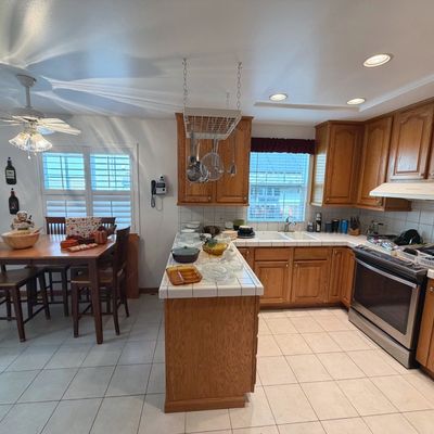 Sale Photo Thumbnail #55: Spacious kitchen featuring oak cabinetry, tile countertops, stainless steel appliances, and a matching dining table with chairs.