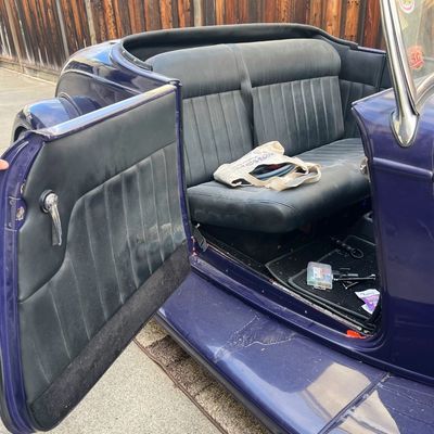 Sale Photo Thumbnail #25: Interior view of a vintage dark purple hot rod roadster, featuring black tufted upholstery, open door panel, and a bench seat.