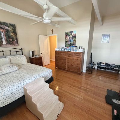 Sale Photo Thumbnail #50: Spacious bedroom featuring a wrought iron bed frame, a large wooden dresser with multiple drawers, carpeted pet stairs, and framed artwork on beige walls.