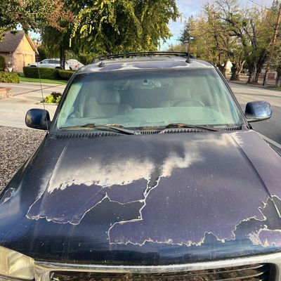 Sale Photo Thumbnail #34: Front view of a dark blue GMC SUV showing significant clear coat peeling and paint damage on the hood and roof.