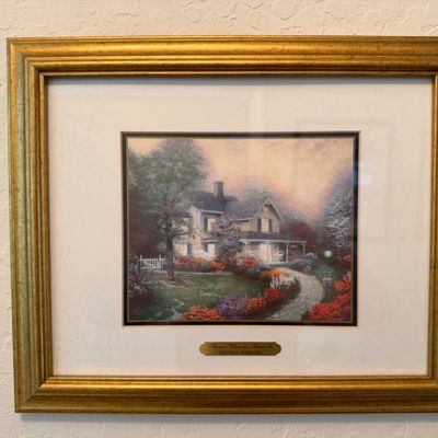 Sale Photo Thumbnail #2: Framed Thomas Kinkade print titled "Home is Where the Heart Is", presented in a gold-finished wood frame with a double mat and title plaque.
