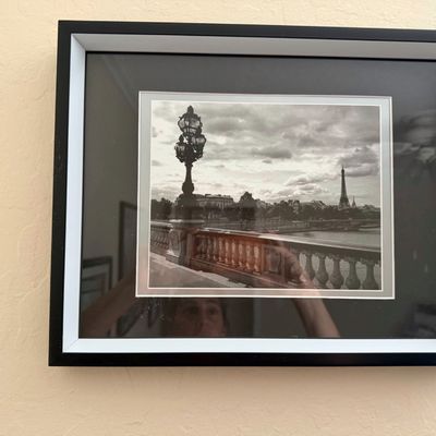 Sale Photo Thumbnail #19: Framed black and white photograph featuring a Parisian bridge scene with the Eiffel Tower in the distance, set in a dark-matted black and white frame.