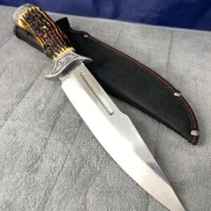 Fixed-blade Bowie style knife featuring a stag horn handle, ornate metal bolster, and a black nylon sheath.