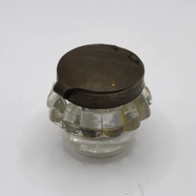 Sale Photo Thumbnail #61: Antique clear pressed glass inkwell featuring a ribbed body and a hinged metal lid with a aged patina.
