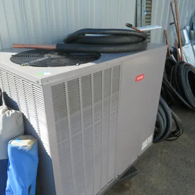 Sale Photo Thumbnail #50: Bryant brand outdoor HVAC condenser unit, shown with copper tubing coiled on top alongside additional piping and ductwork.