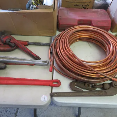 Sale Photo Thumbnail #37: Selection of heavy-duty hand tools including several pipe wrenches, a large coil of copper tubing, and vintage metal hardware.