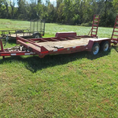 Sale Photo Thumbnail #64: Red Mid-Atlantic dual-axle flatbed equipment trailer with wooden deck, fold-up rear ramps, and a smaller utility trailer parked behind it.