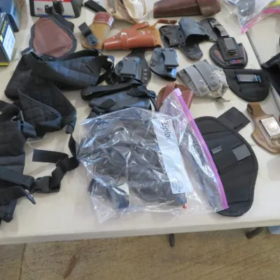 Sale Photo Thumbnail #59: Assortment of leather and nylon gun holsters, tactical gear, and accessories displayed on a table.
