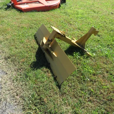 Sale Photo Thumbnail #62: Yellow three-point hitch rear grader blade for a tractor, showing light wear and minor rust. An orange rotary cutter attachment is partially visible in the background.